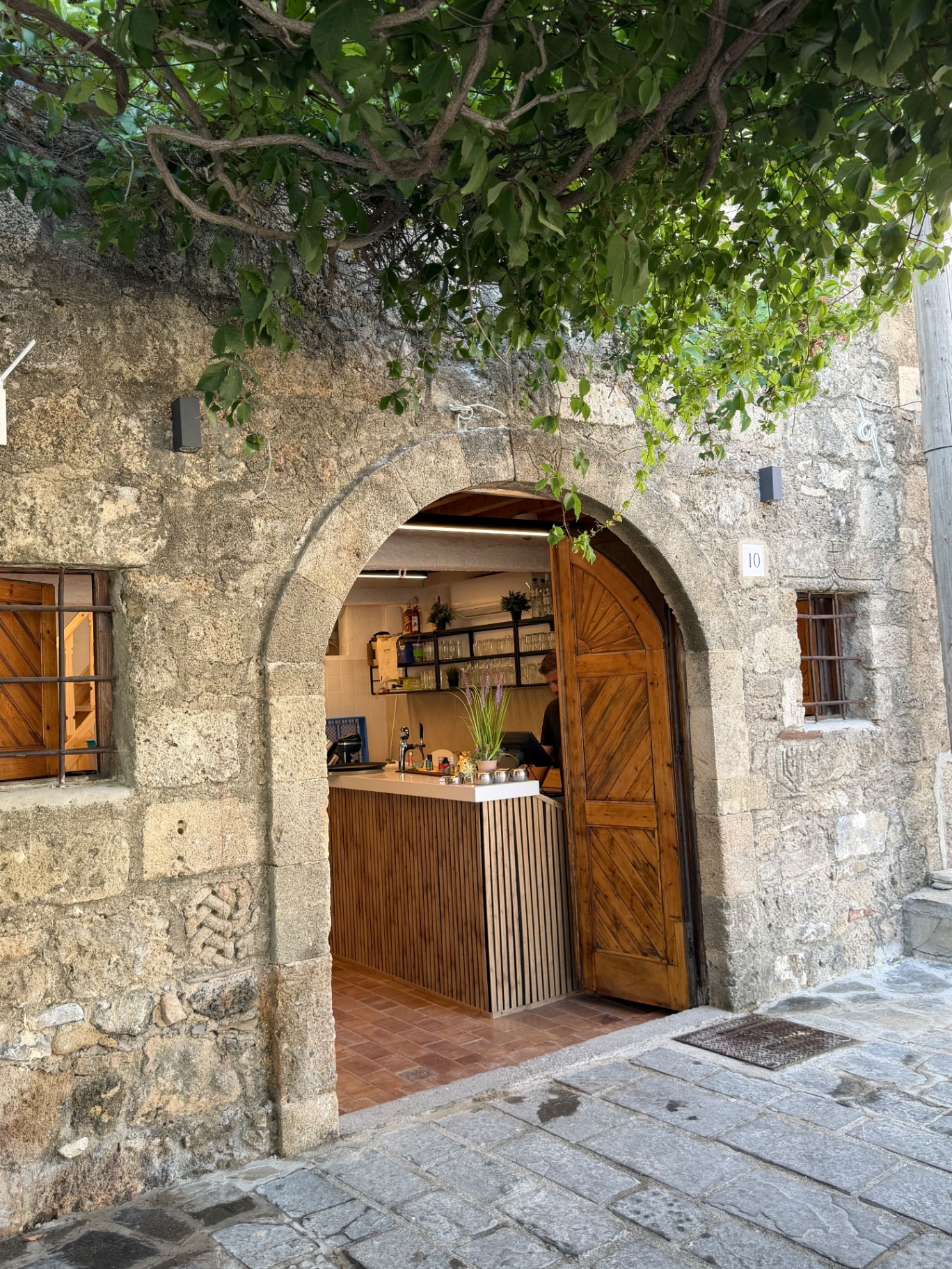 The arched stone entrance of Lindos Boathouse with the bar visible inside, framed by mulberry leaves